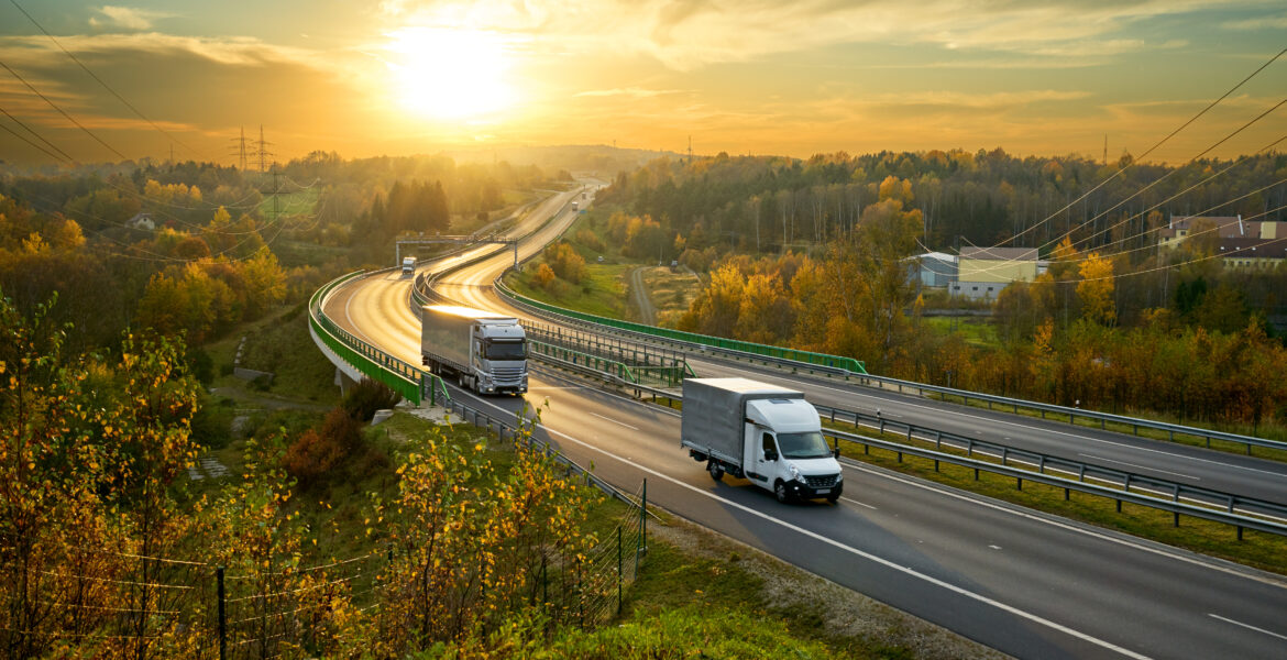 Delivery van and truck driving on the highway winding through forested landscape in autumn colors at sunset