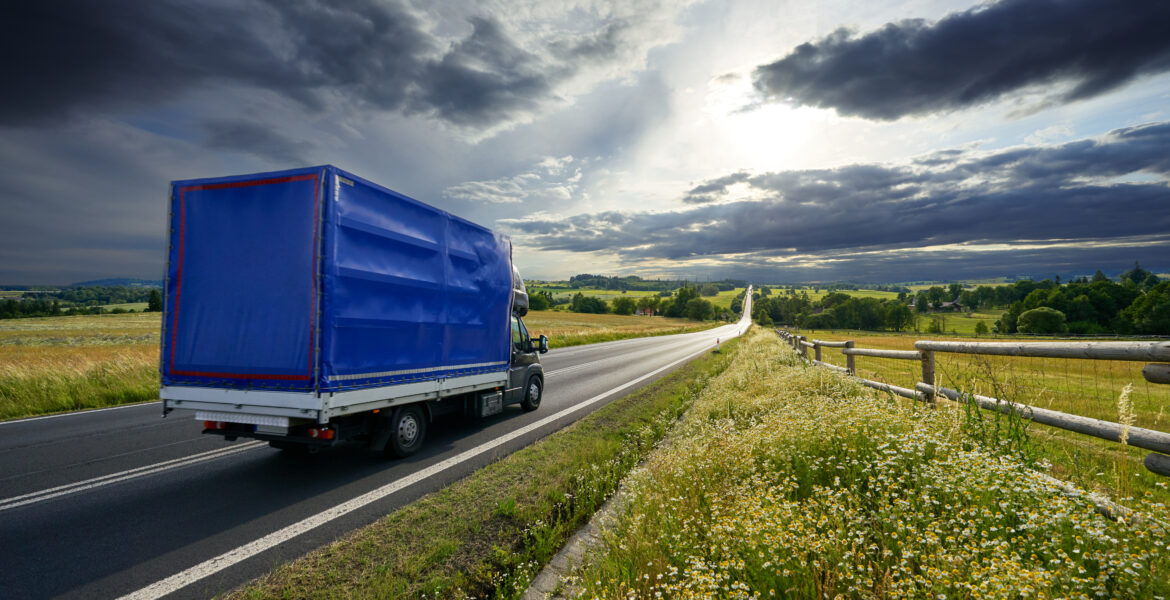 Delivery van driving on the asphalt road in rural landscape at sunset with dramatic clouds